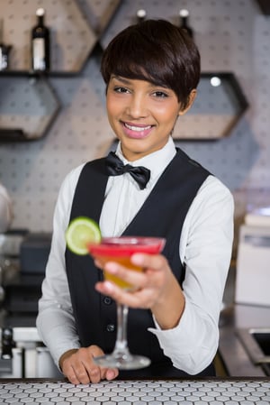 Portrait of smiling bartender holding glass of cocktail in bar counter at bar